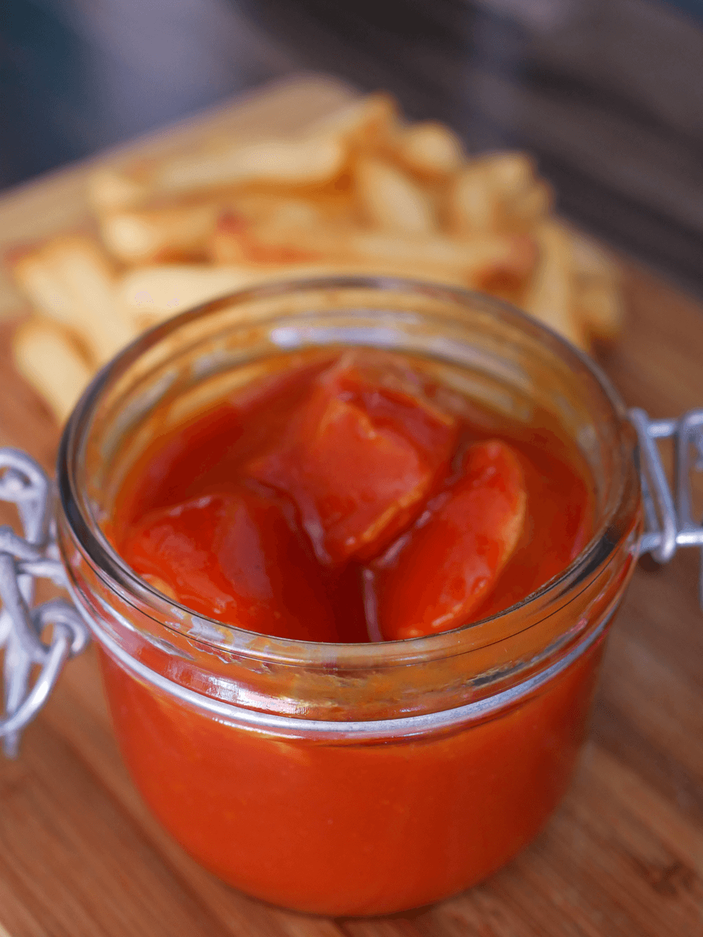 Ästhetische Draufsicht auf ein offenes Glas Berliner Currywurst, saftige Wurststücke in kräftiger roten Ketchup mit super crunchy Pommes.